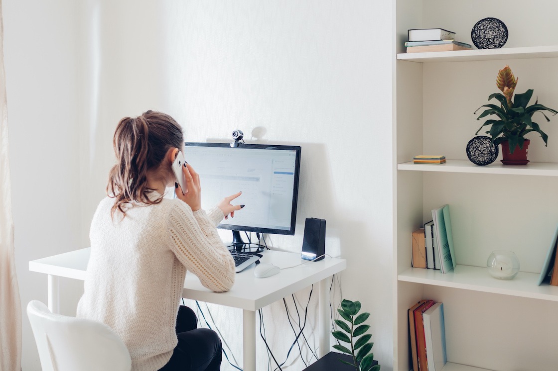 Work from home during coronavirus pandemic. Woman stays home talking on phone. Workspace of freelancer. Office interior with computer