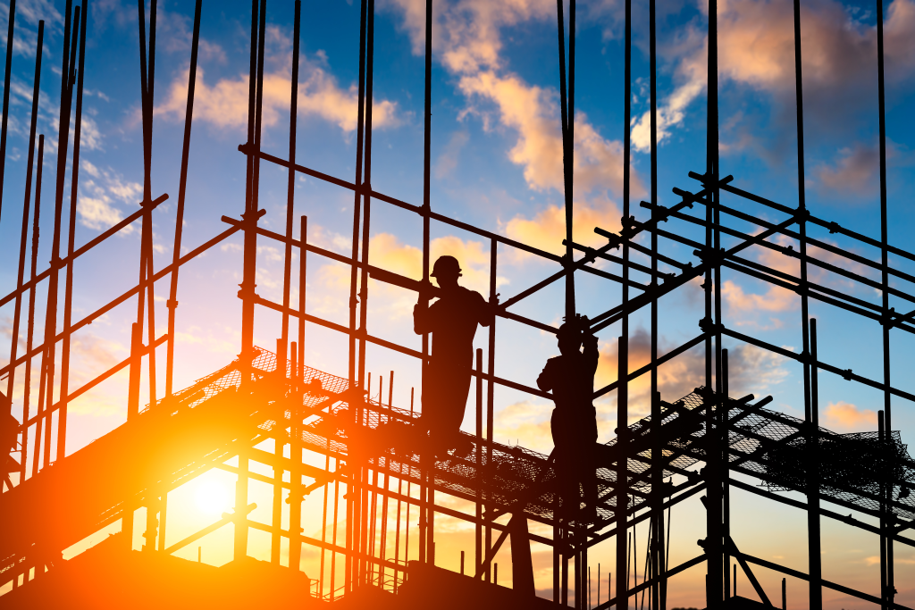 Silhouetted workers on scaffolding at a construction site during sunset, installing structural framework